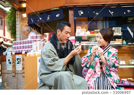 A photo of a couple eating food and having fun together beside a small store. 33006997