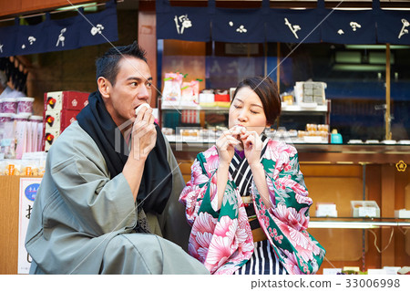 A young couple is sitting and eating together outside. A young couple is sitting and eating together outside. 33006998