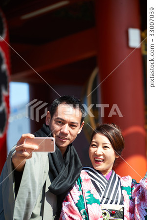 a photo of a couple in kimono smiling and taking a photo. 33007039
