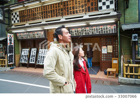 a photo of a couple walking and looking at something on a street 33007066