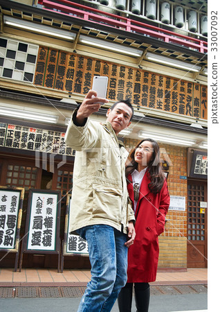 a couple is standing outdoors and taking selfie 33007092