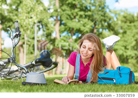 Young woman reading a book after cycling at the 33007859