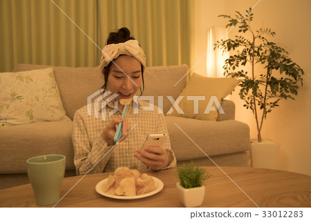 Woman eating potato chips with tongs at night while looking at a smartphone 33012283