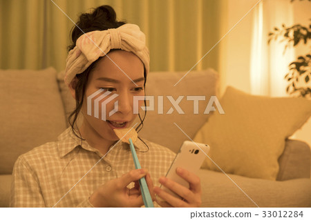 Woman eating potato chips with tongs at night while looking at a smartphone 33012284