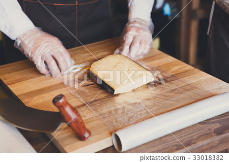 Shop assistant wrapping a piece of cheese Shop assistant wrapping a piece of cheese 33018382