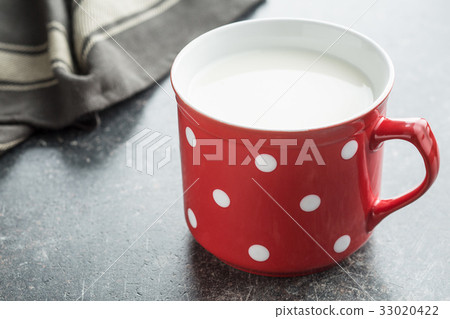 Milk in red mug with white spots. 33020422