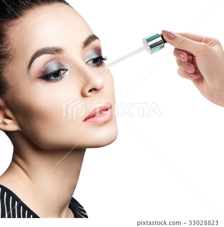 Cosmetic oil applying on face of young woman. Cosmetic oil applying on face of young woman. 33028823