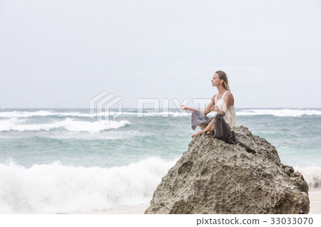 Girl sit at the seaside on the rock and meditating Girl sit at the seaside on the rock and meditating 33033070