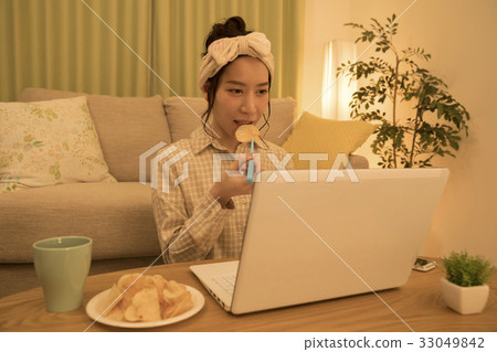 Woman eating potato chips with tongs at night while working on a computer Woman eating potato chips with tongs at night while working on a computer 33049842