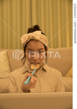 Woman eating potato chips with tongs at night while working on a computer 33050425