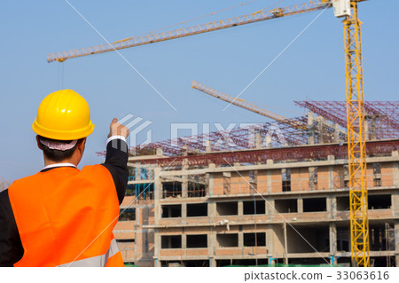 engineer orange shirt stands pointing at building engineer orange shirt stands pointing at building 33063616