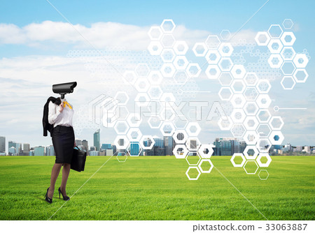 Camera headed woman standing on green grass against modern cityscape 33063887