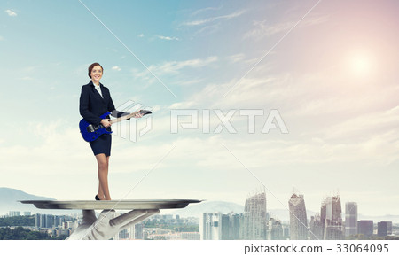 Attractive businesswoman on metal tray playing electric guitar against cityscape background Attractive businesswoman on metal tray playing electric guitar against cityscape background 33064095