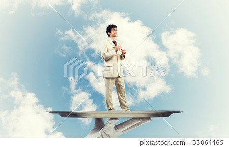 Businessman on metal tray playing fife against blue sky background 33064465