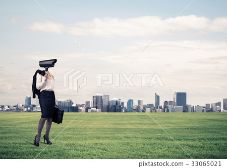 Camera headed woman standing on green grass against modern citys 33065021