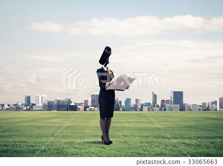 Camera headed woman standing on green grass against modern citys 33065663