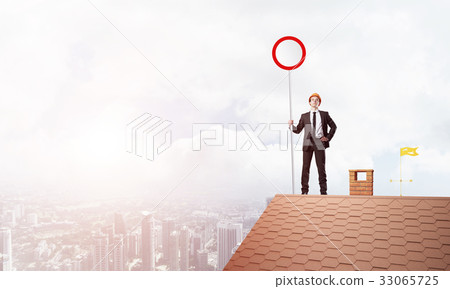 Caucasian businessman on brick house roof showing stop road sign. Mixed media Caucasian businessman on brick house roof showing stop road sign. Mixed media 33065725