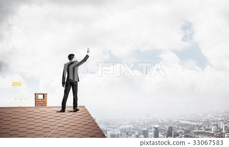 Businessman on house roof touch empty space. Mixed media 33067583