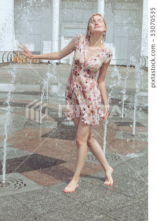Woman is playing in the fountain with a spray. 33070535