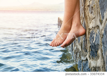 Bare girl's feet dangling from the stone jetty 33074334