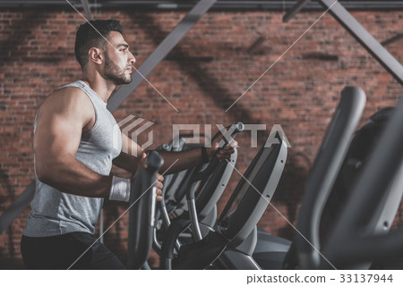 Serene unshaven athlete making exercise in gym Serene unshaven athlete making exercise in gym 33137944