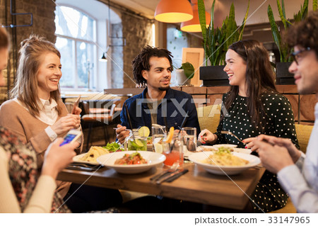 friends with smartphones eating at restaurant 33147965
