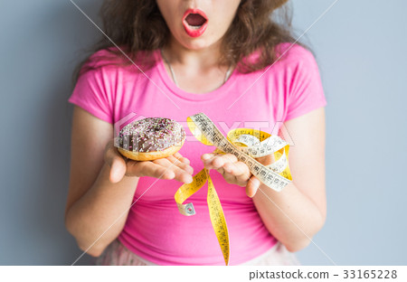Confused young woman holding a donut and a 33165228