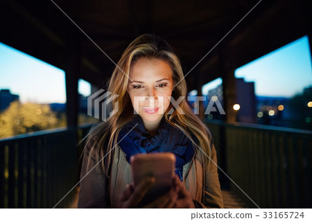 Woman in the city at night holding smartphone 33165724