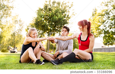 Group of young runners sitting on grass stacking Group of young runners sitting on grass stacking 33166096