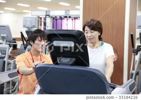 Elderly woman getting advice from coach while walking in sports club 33184216