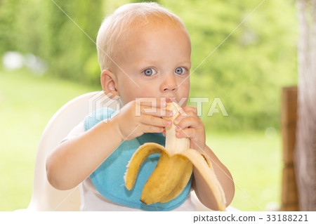 Cute baby boy in a blue bip eating a banana 33188221