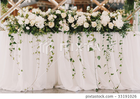 Green branches hang from white rose garland  33191026