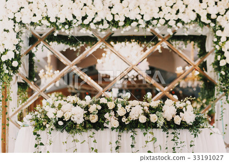 Green branches hang from white rose garland  33191027