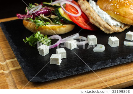 Open hamburger lies on the slate tile. 33199898