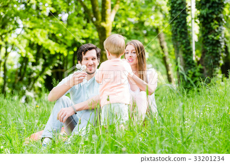 Little boy running over meadow with family in back 33201234
