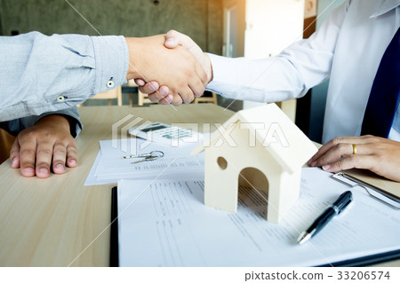 Estate agent in suit sitting in an office desk shaking hands wit Estate agent in suit sitting in an office desk shaking hands wit 33206574