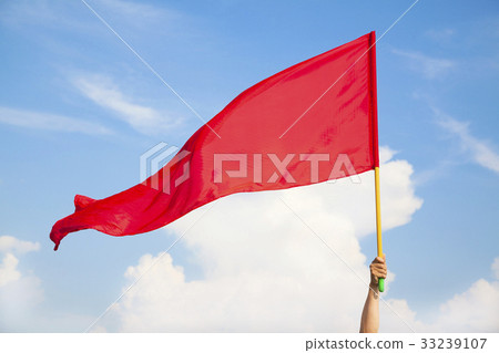 Hand waving a red flag with blue sky background Hand waving a red flag with blue sky background 33239107