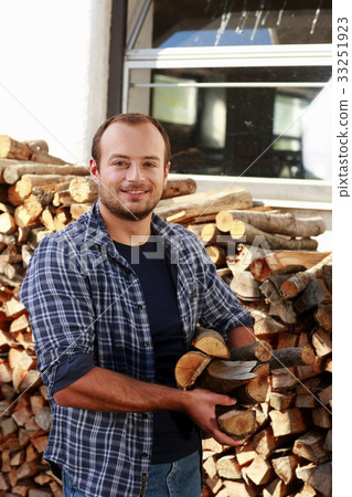 farmer carries firewood in front of a woodpile 33251923
