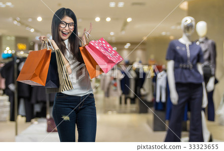 Happy young asian woman shopping in happy feeling and holding the product paper bag over the Abstract blurred photo of clothing store in a shopping mall, shopping concept Happy young asian woman shopping in happy feeling and holding the product paper bag over the Abstract blurred photo of clothing store in a shopping mall, shopping concept 33323655