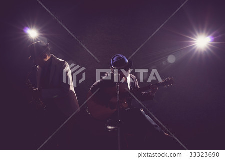 Musician Duo band playing a saxophone and singing a song and playing the guitar on black background with spot light and lens flare, musical concept Musician Duo band playing a saxophone and singing a song and playing the guitar on black background with spot light and lens flare, musical concept 33323690