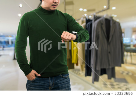 A guy wearing blank mock neck long t-shirt while standing and seeing the clock over the Abstract blurred photo of clothing store in a shopping mall, shopping concept A guy wearing blank mock neck long t-shirt while standing and seeing the clock over the Abstract blurred photo of clothing store in a shopping mall, shopping concept 33323696