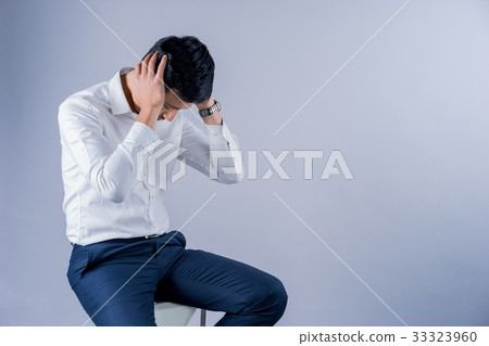 a businessman is sitting and holding his head on gray background a businessman is sitting and holding his head on gray background 33323960