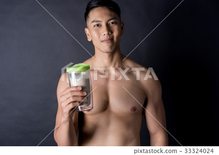 Asian body builder drinking a protein shake on black background Asian body builder drinking a protein shake on black background 33324024
