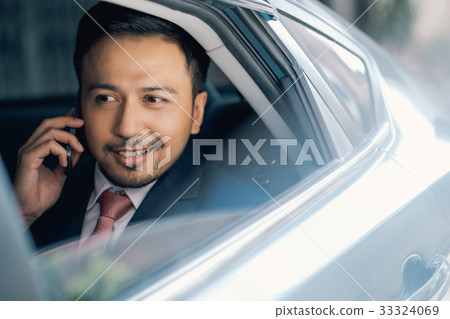Asian handsome businessman is on call in car, smiling and looking outside 33324069