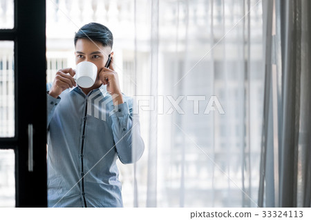 a young man is drinking water and calling indoor 33324113