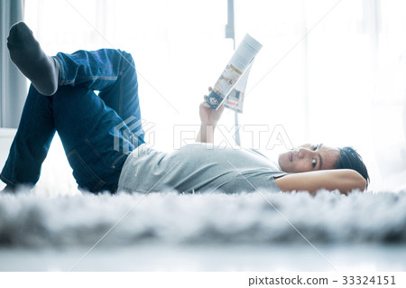 A photo of a man lying and reading newspaper 33324151