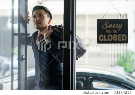 A photo of a businessman opening a door while carrying a bag over his shoulder. 33324235