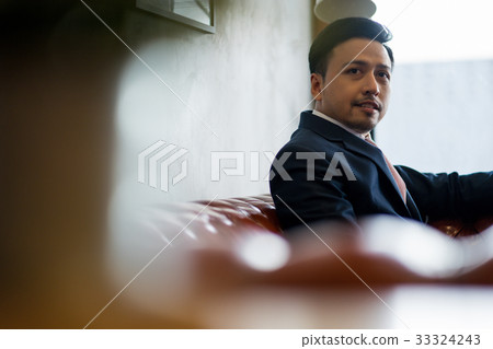 A portrait of businessman sitting on couch and smiling inside. 33324243