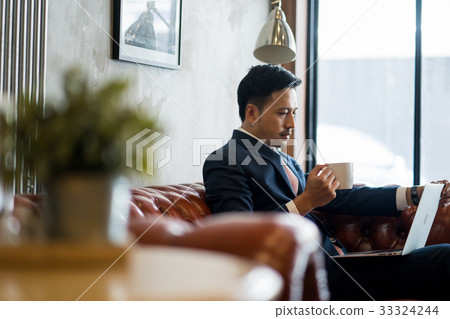 A portrait of young businessman drinking coffee while looking at the laptop. 33324244