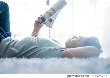 a man is lying on the bed and reading a magazine 33324264